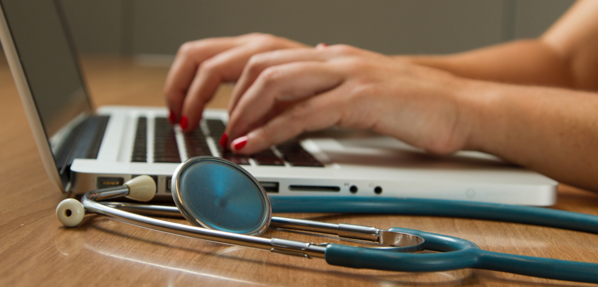 sthéthoscope posé à coté d'un ordinateur portable, avec personne tapant sur le clavier